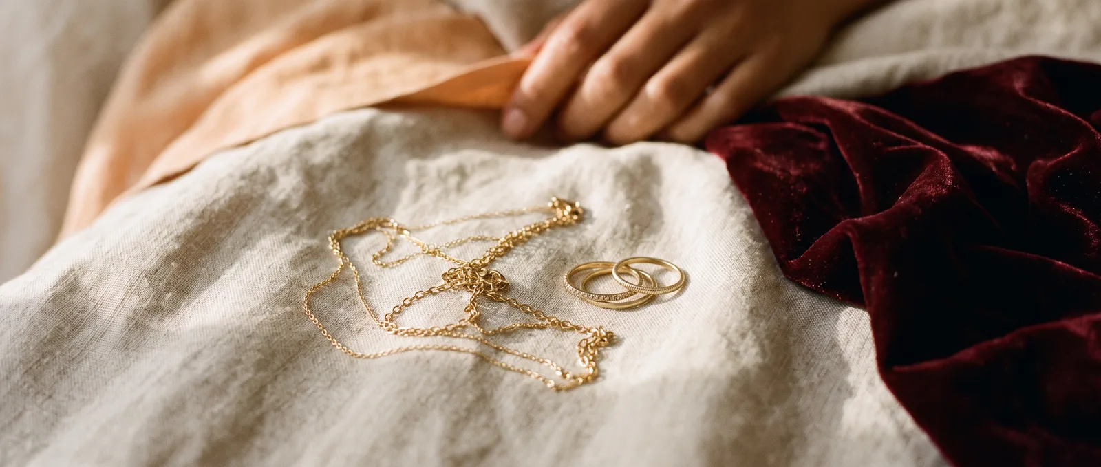 Fine gold chains and slim stacking bands laid on pale linen
