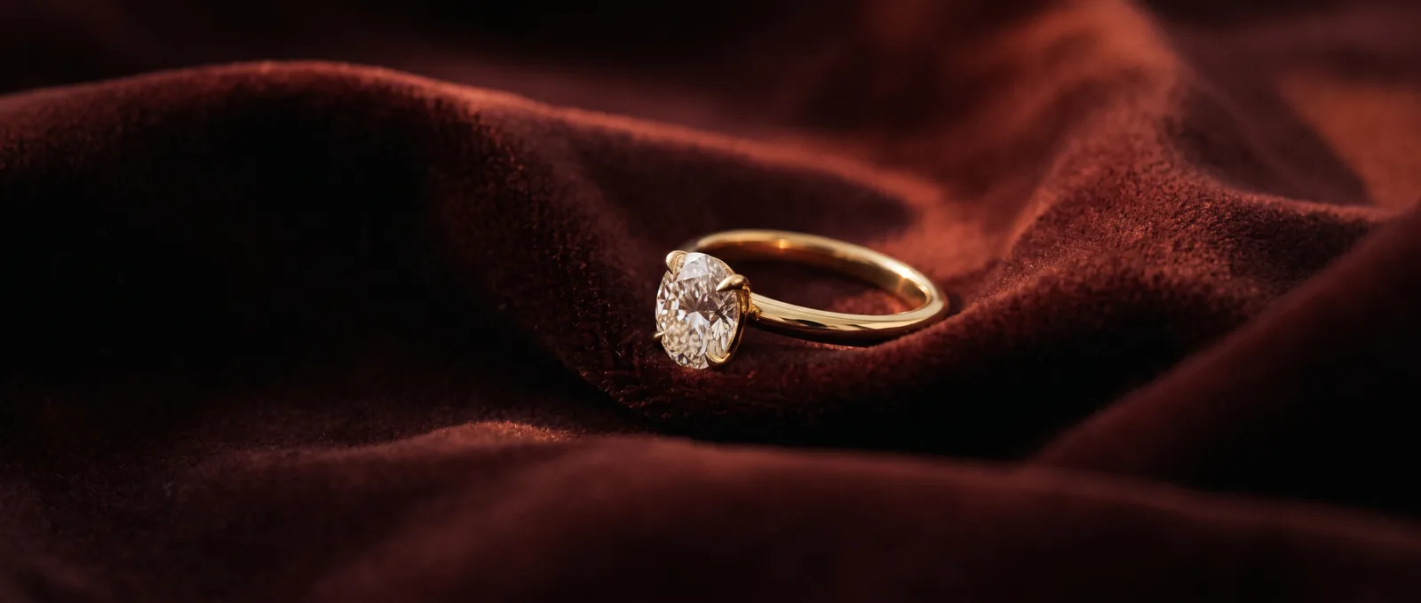 An oval diamond solitaire in yellow gold on oxblood velvet