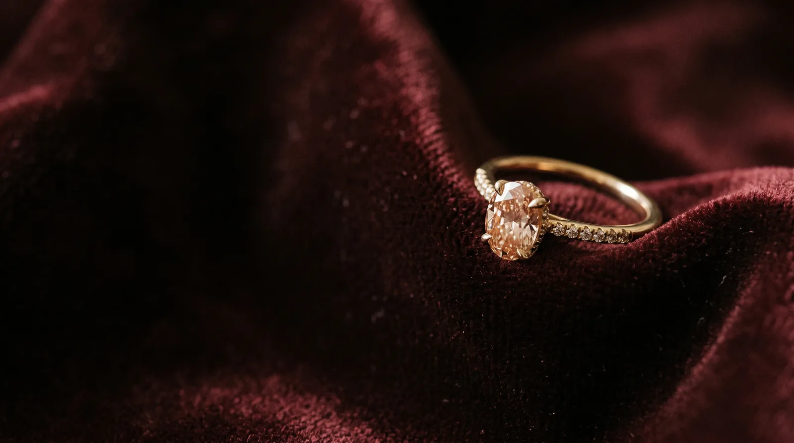 A gold ring with a champagne diamond resting on dark velvet