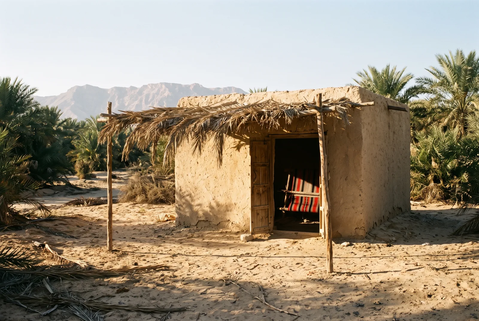 Small mud-brick room with a Sadu loom in the doorway, at the edge of a palm oasis