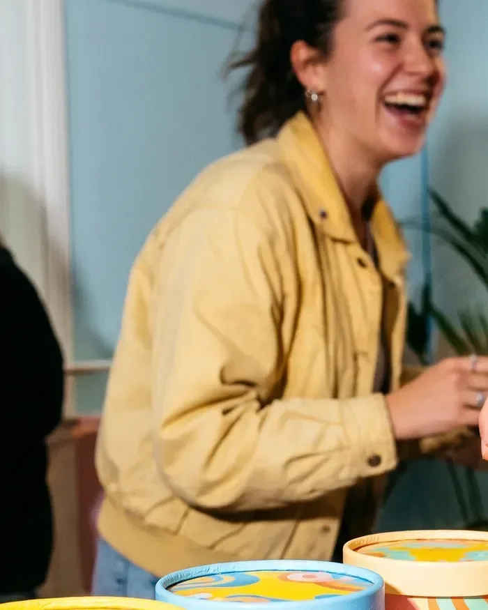 A woman in a yellow jacket laughing over a counter of ice cream tubs
