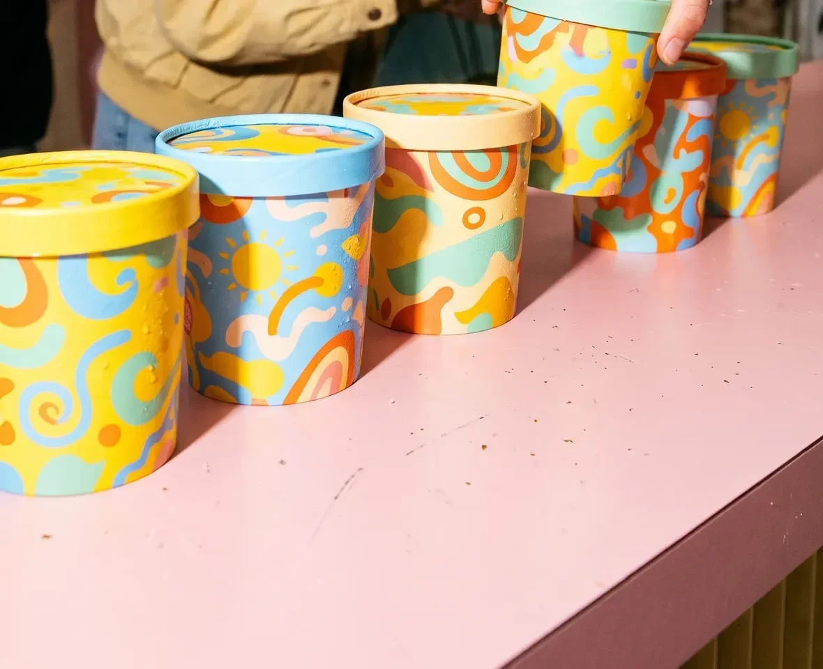 Hands picking colourful ice cream tubs off a pink counter