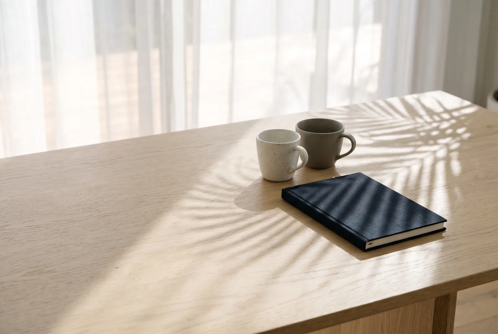 Two coffee cups and a closed notebook on a table in the afternoon sun