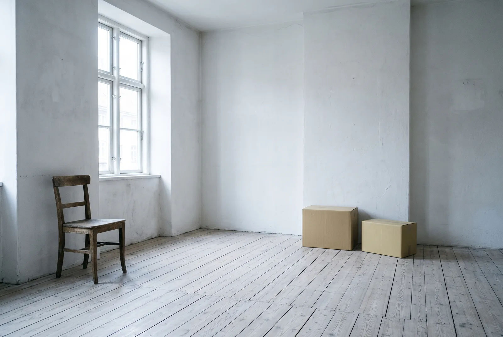 A bright, nearly empty room with one wooden chair by a tall window
